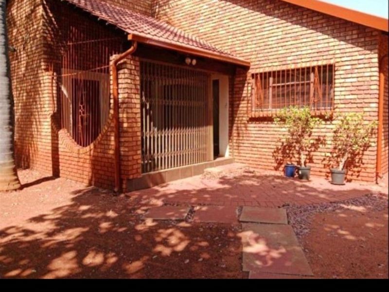 A rear exterior view of a face brick house featuring a paved patio area, security gates, and security bars on the windows.