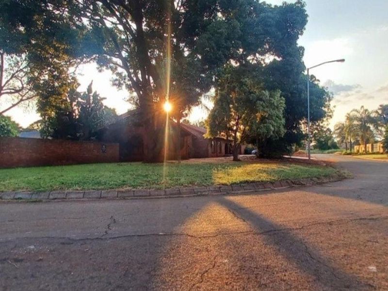 A street-level view of the property frontage, featuring a brick boundary wall, mature trees, and asphalt road access in a residential neighbourhood.