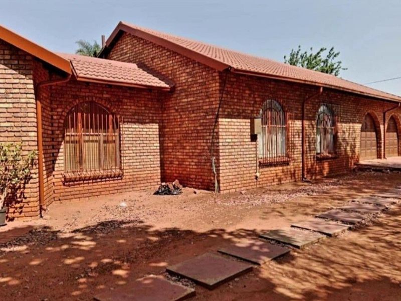 Rear exterior view of a face brick house featuring arched windows with security bars and a tiled roof, set against an unlandscaped yard.