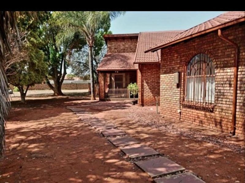 A view of the rear exterior featuring a face-brick facade, tiled roof, and a stone paver pathway leading toward the house entrance.