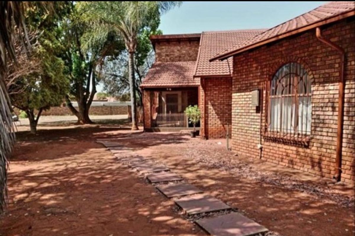 A view of the rear exterior featuring a face-brick facade, tiled roof, and a stone paver pathway leading toward the house entrance.