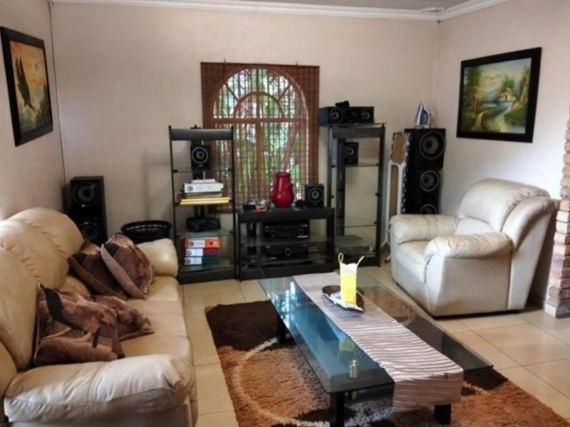 A living room featuring tiled flooring, an arched window with security bars, and decorative cove cornicing.