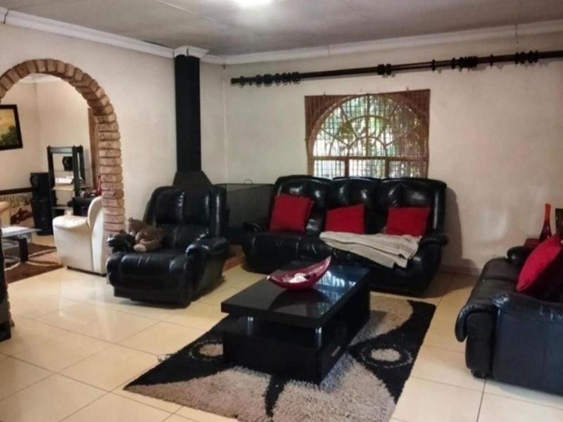 Spacious living room featuring a distinctive brick archway, tiled flooring, and a built-in fireplace, offering a traditional layout with potential for modernization.