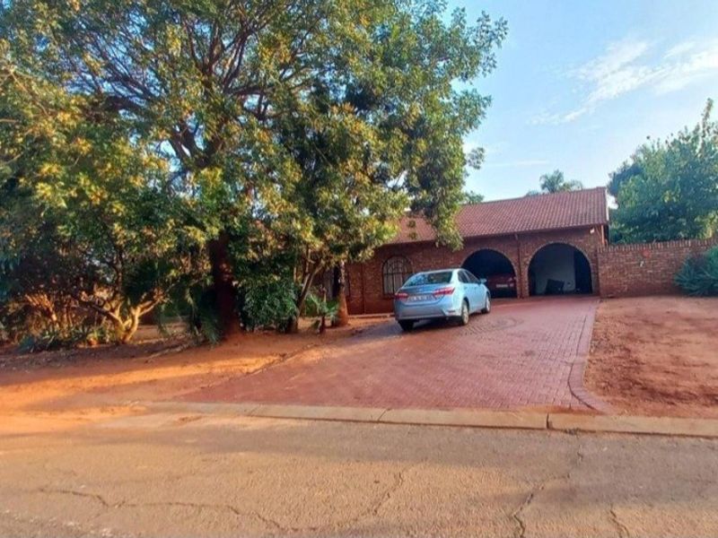Front view of a facebrick house featuring a paved driveway, double arched garage, and established trees on a large plot.