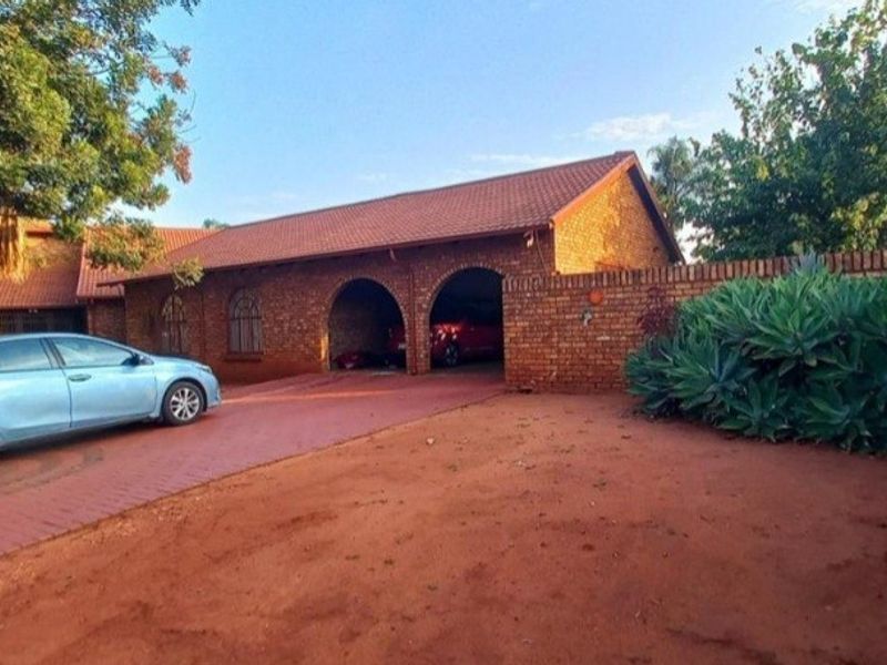 Front exterior view of a brick house featuring a tiled roof, arched garage bays, and a paved driveway enclosed by a brick boundary wall.