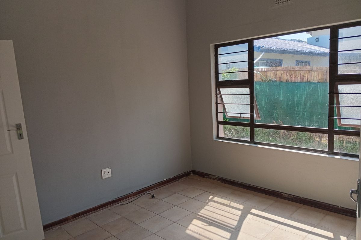 An empty bedroom featuring tiled flooring, metal window frames with security bars, and neutral wall paint, awaiting personal touches.
