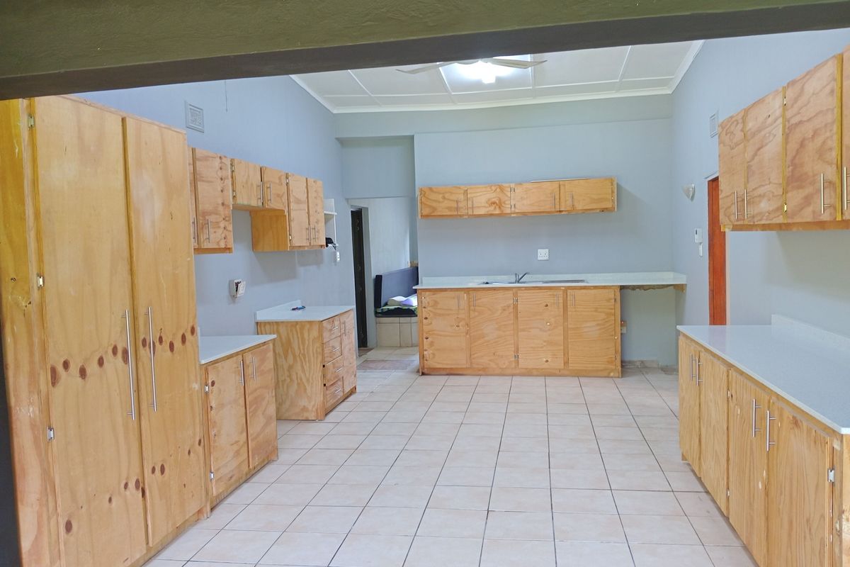 Spacious kitchen featuring extensive unfinished plywood cabinetry, laminate countertops, a stainless steel sink, and neutral tiled flooring.