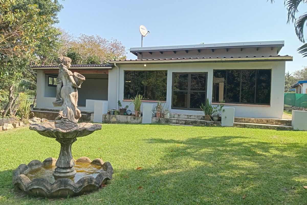 Rear view of the house featuring a spacious lawn, a stone fountain, and a covered patio area with large windows.