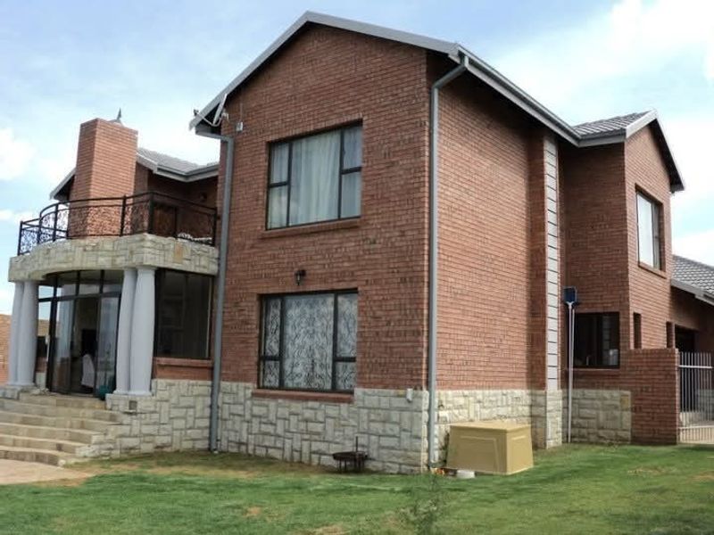 Rear view of a double-story brick house featuring stone cladding, a balcony with wrought iron railings, and a well-maintained lawn.