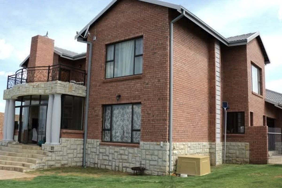 Rear view of a double-story brick house featuring stone cladding, a balcony with wrought iron railings, and a well-maintained lawn.