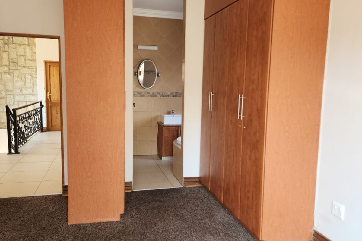 Spacious bedroom featuring built-in wooden cupboards, crown molding, a ceiling fan, and direct access to an en-suite bathroom.