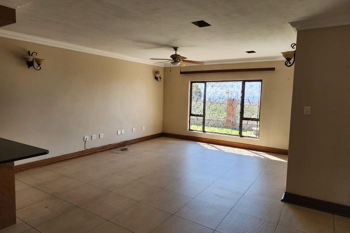 Spacious, empty living area featuring tiled flooring, ceiling fan, and large windows with decorative security bars, offering a blank canvas for interior design.