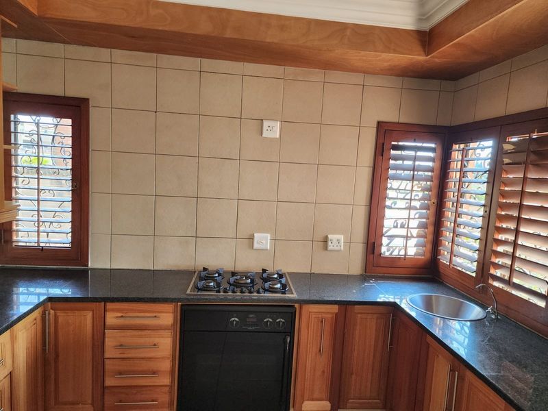 A well-maintained kitchen featuring wooden cabinetry, granite countertops, a built-in oven with gas hob, and classic wooden shutters.