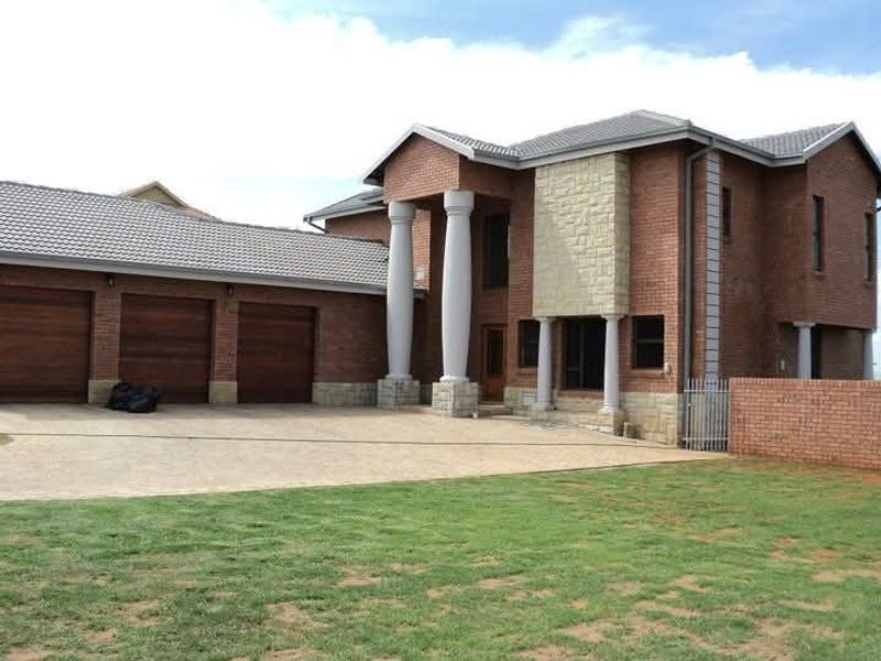 A substantial double-story brick residence featuring a triple garage, stone-clad accents, and prominent architectural columns, set on a paved driveway with a lawn.