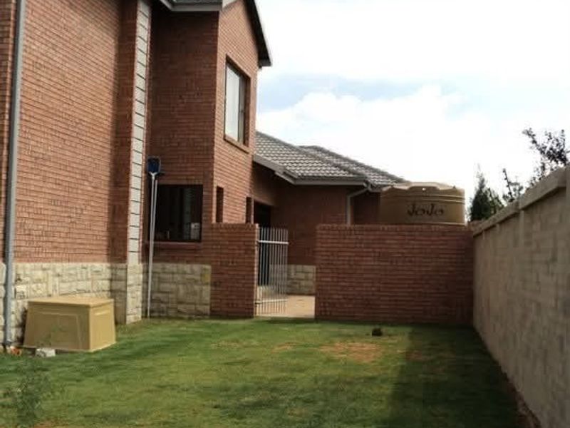 Rear view of a face brick house featuring stone cladding, a tiled roof, a private garden area, and a water storage tank.