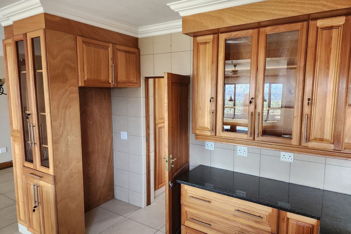 A clean kitchen featuring warm-toned wooden cabinetry, granite countertops, tiled backsplash, and ample storage space with glass-front display units.
