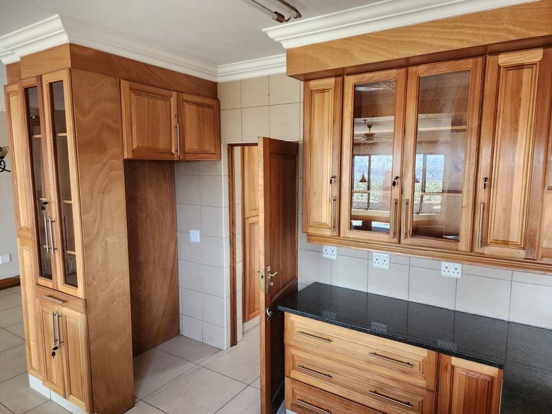 A clean kitchen featuring warm-toned wooden cabinetry, granite countertops, tiled backsplash, and ample storage space with glass-front display units.