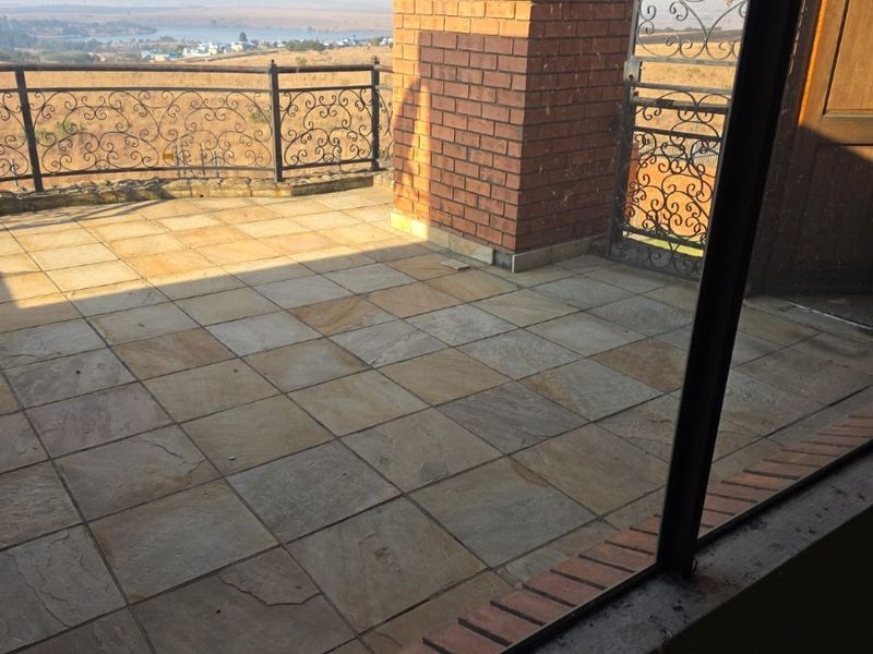 An elevated balcony featuring stone tile flooring, a brick pillar, and decorative wrought iron balustrades with expansive landscape views.
