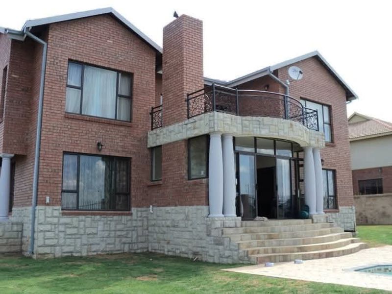 Rear elevation of a double-story brick house featuring stone cladding, a balcony with wrought iron railings, and a paved patio area.