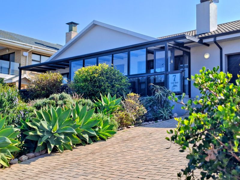 Front elevation of the property featuring a paved driveway, an enclosed patio area, and a well-maintained garden entrance.