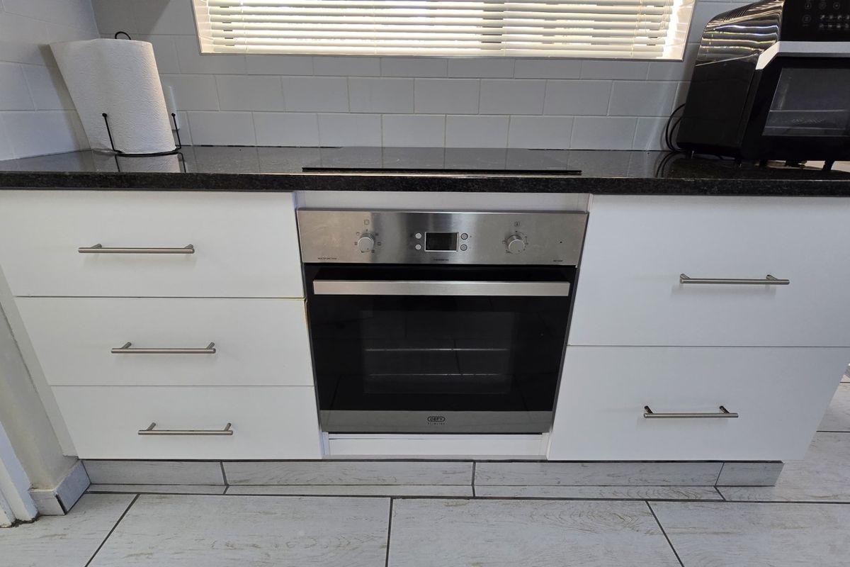 Modern kitchen featuring white cabinetry, granite countertops, subway tile backsplash, and a built-in electric oven with a sleek hob.