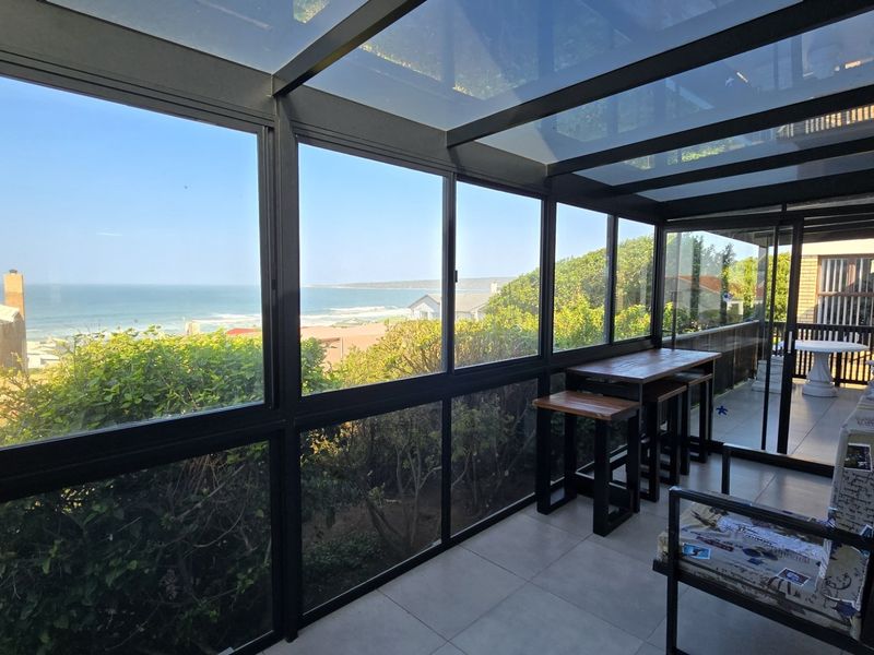 Enclosed patio featuring a glass roof, black aluminum framing, and tiled flooring, offering expansive ocean views.