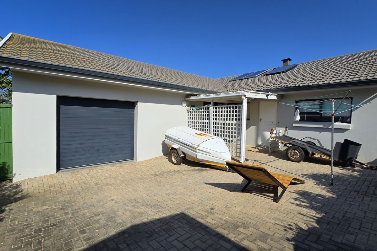 Rear exterior view of the property featuring a paved courtyard, garage access, and a covered patio area with solar panels installed on the roof.