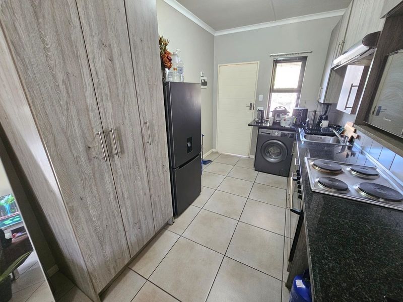 A functional kitchen featuring wood-look cabinetry, granite countertops, an electric hob, and tiled flooring with space for laundry appliances.