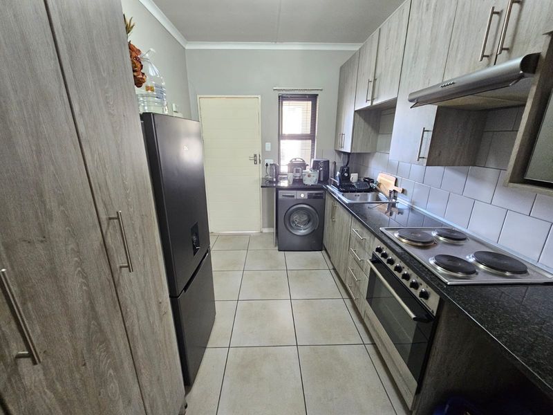 A functional galley-style kitchen featuring modern wood-grain cabinetry, granite countertops, a built-in oven with electric hob, and tiled flooring.