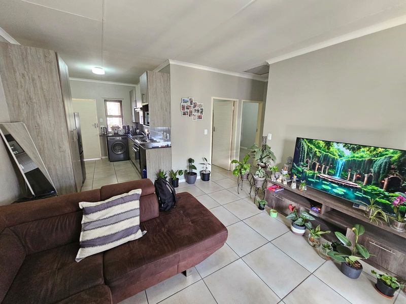 An open-plan living area featuring tiled flooring, a modern kitchen with built-in cabinetry, and direct access to adjacent rooms.