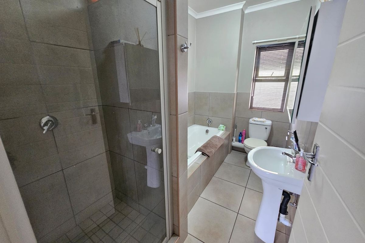 A functional bathroom featuring a glass-enclosed shower, a pedestal basin, a built-in bathtub, and neutral tiled finishes throughout.