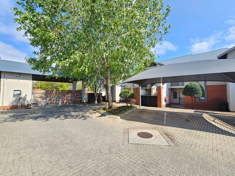 Front exterior view of the townhouse complex featuring a paved driveway, shade sail carport, and secure gated entrance.