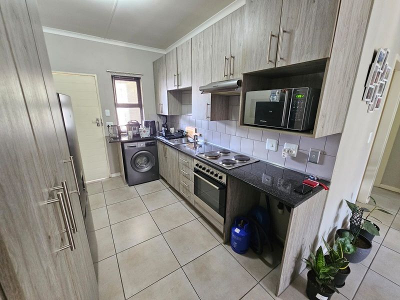 Functional kitchen featuring wood-look cabinetry, granite countertops, built-in oven and hob, extractor fan, and tiled flooring with integrated laundry plumbing.