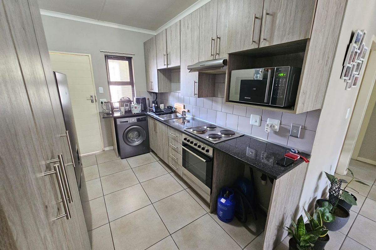 Functional kitchen featuring wood-look cabinetry, granite countertops, built-in oven and hob, extractor fan, and tiled flooring with integrated laundry plumbing.
