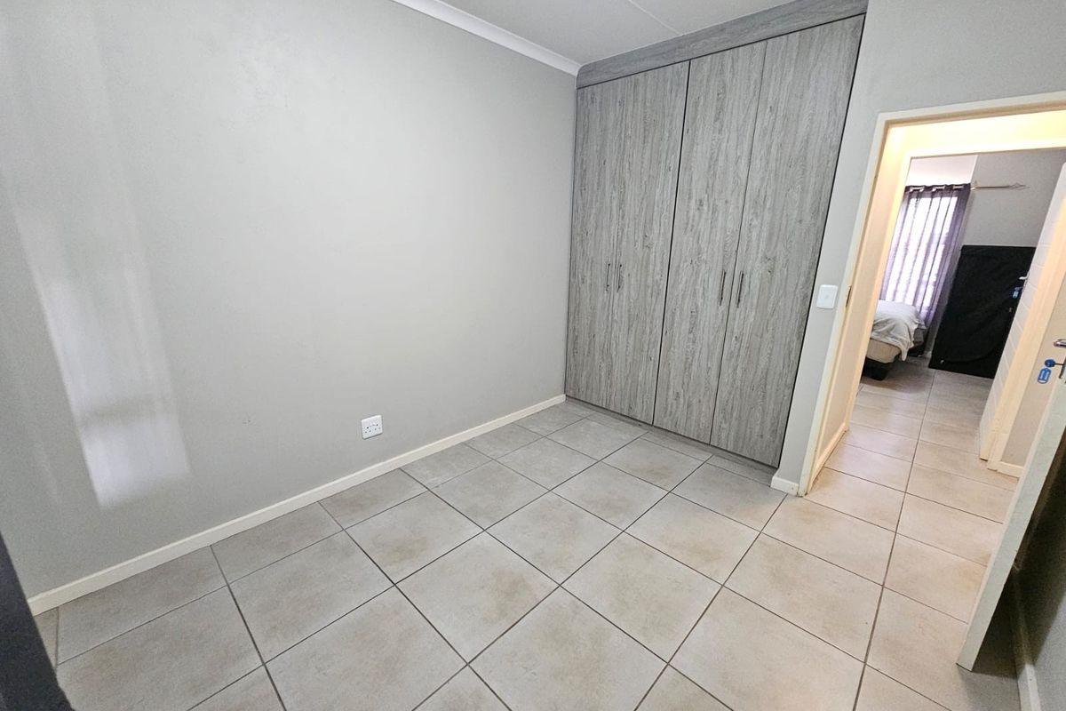 A clean, empty bedroom featuring neutral grey walls, modern wood-look built-in cupboards, and durable tiled flooring.