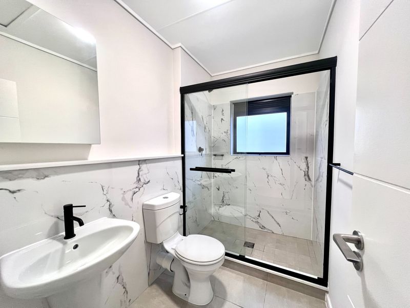 Modern bathroom featuring marble-look wall tiles, a glass shower enclosure with black framing, a pedestal basin with black fixtures, and a toilet.