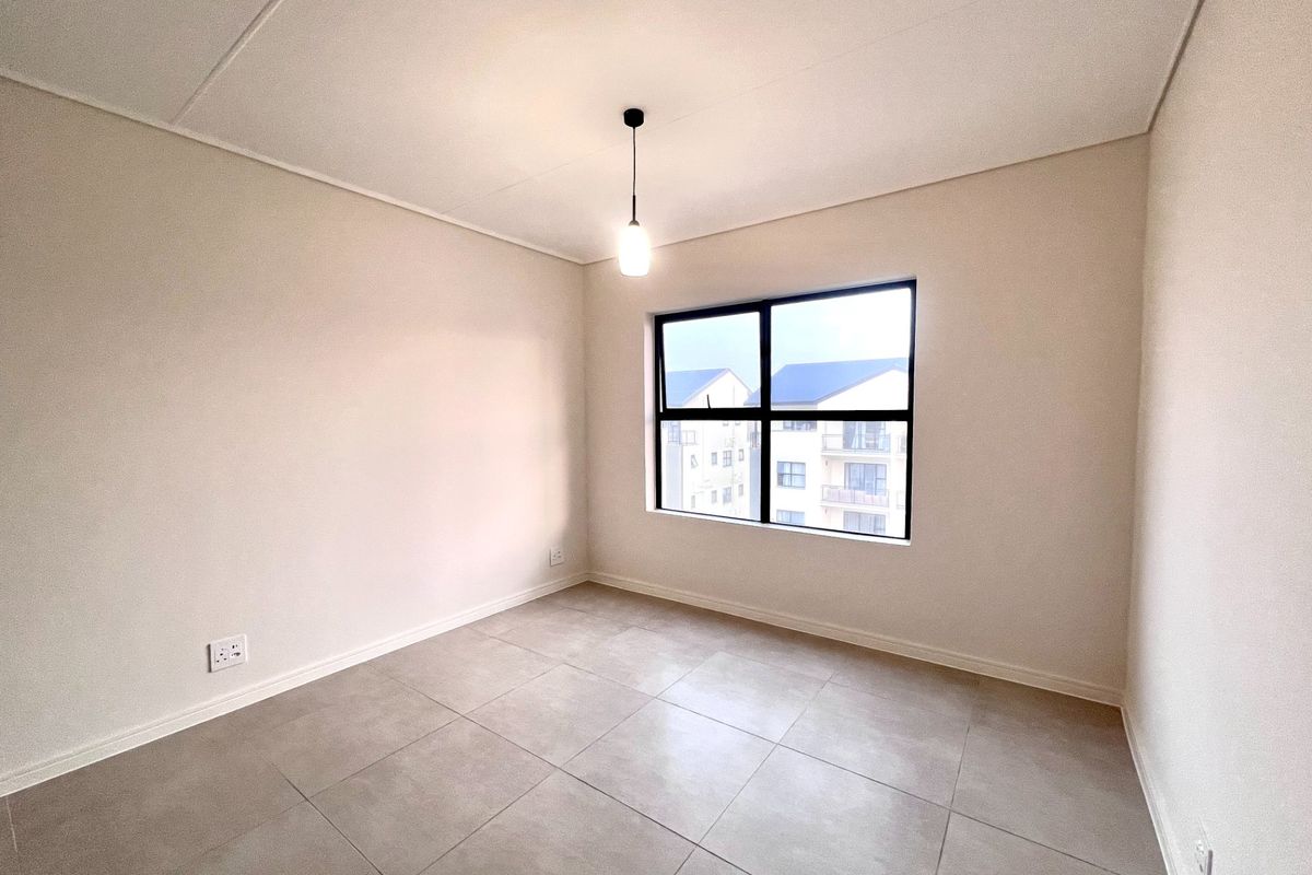 A bright, empty bedroom featuring neutral tiled flooring, a modern black-framed window, and a simple pendant light fixture.