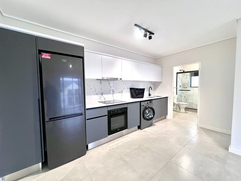 Modern kitchen featuring sleek grey and white cabinetry, marble-look splashback, integrated appliances, and tiled flooring, with an adjacent bathroom visible.