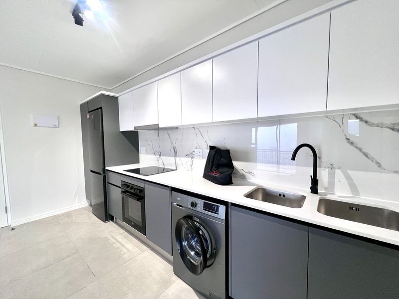 Modern kitchen featuring sleek grey and white cabinetry, marble-look splashback, quartz countertops, and integrated appliances including an oven, hob, and washing machine.