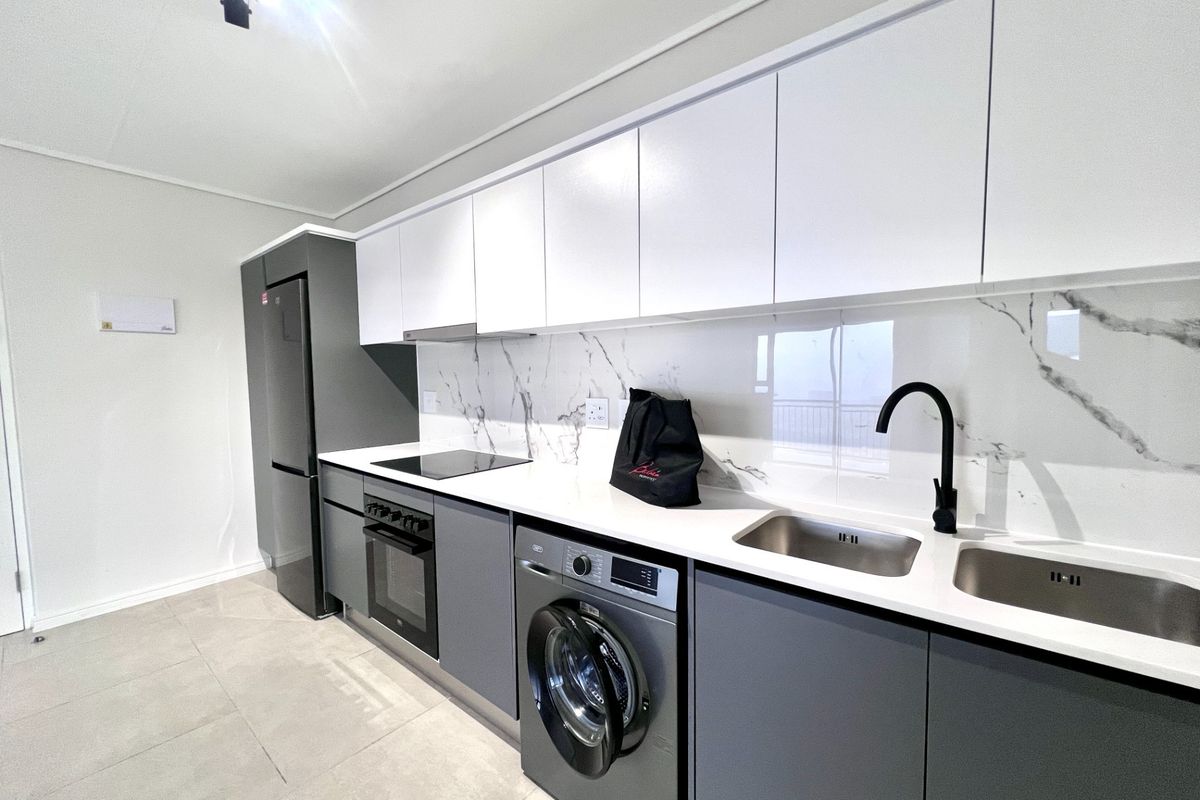 Modern kitchen featuring sleek grey and white cabinetry, marble-look splashback, quartz countertops, and integrated appliances including an oven, hob, and washing machine.