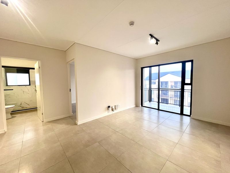 A bright, modern, and empty living area featuring large format floor tiles, neutral walls, and a sliding glass door leading to a private balcony.