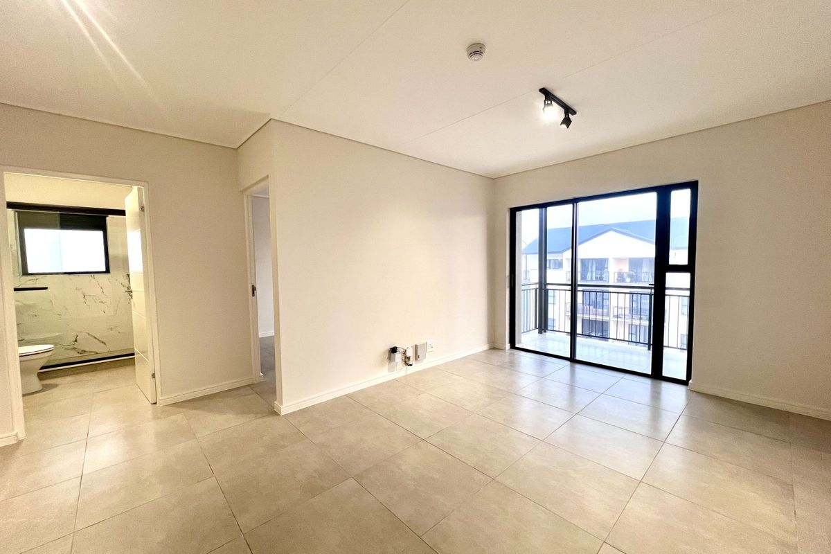 A bright, modern, and empty living area featuring large format floor tiles, neutral walls, and a sliding glass door leading to a private balcony.
