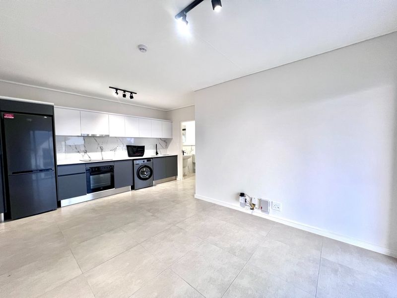 Modern open-plan kitchen featuring sleek two-tone cabinetry, marble-look backsplash, integrated appliances, and neutral tiled flooring in a bright, well-maintained space.