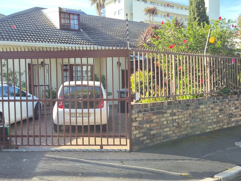 Front elevation of a residential house featuring a tiled roof, brick boundary wall, and secure metal gate with electric fencing.