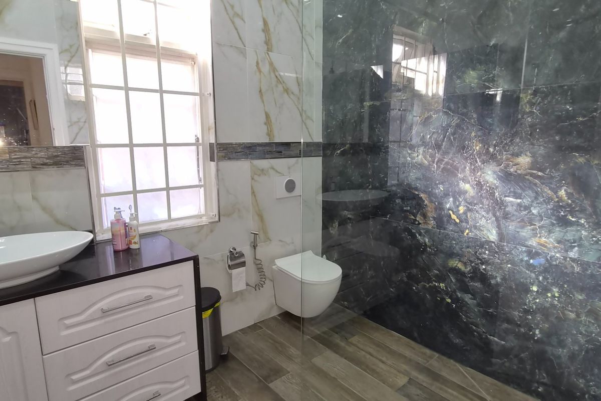Modern bathroom featuring a wall-mounted toilet, vessel sink vanity, and a spacious walk-in shower with striking dark marble-effect wall tiles.