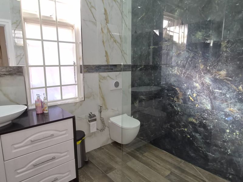 Modern bathroom featuring a wall-mounted toilet, vessel sink vanity, and a spacious walk-in shower with striking dark marble-effect wall tiles.
