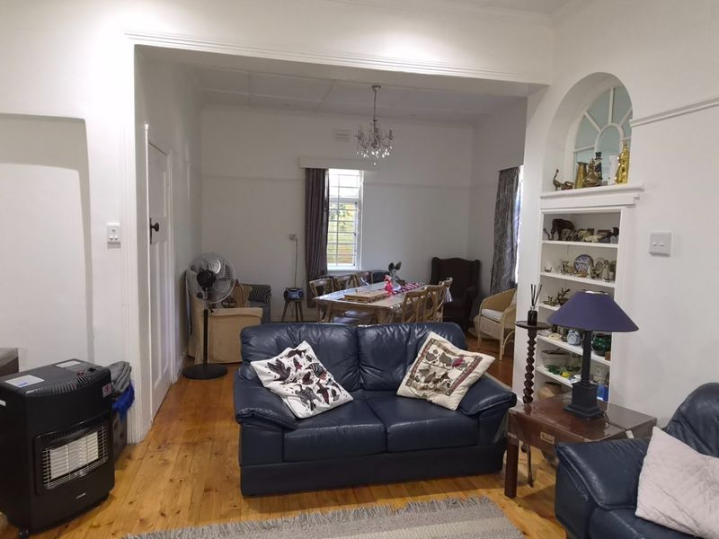 Open plan living and dining area featuring polished timber flooring, built-in shelving, and classic architectural details including picture rails and an arched window.