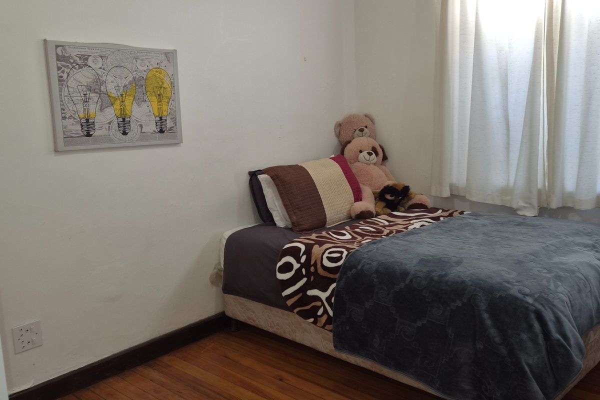 A compact bedroom featuring hardwood flooring and neutral wall finishes, offering a functional space with natural light from the window.