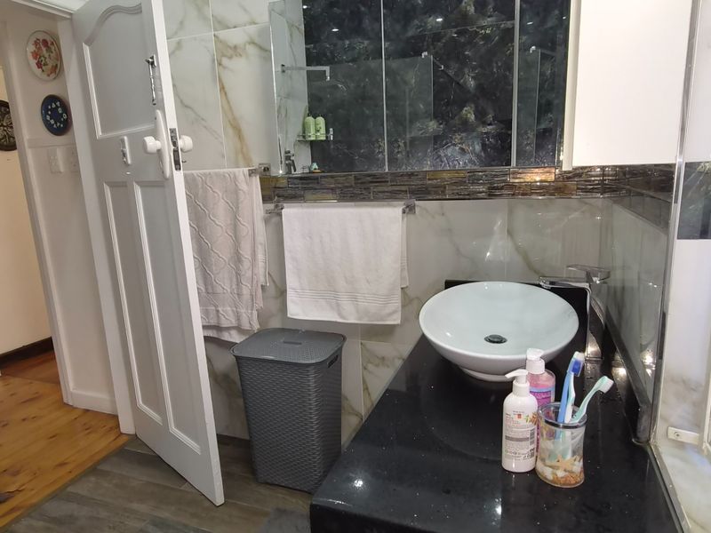 A modern bathroom featuring a vessel sink set on a black granite vanity, complemented by marble-look wall tiles and a glass shower enclosure.