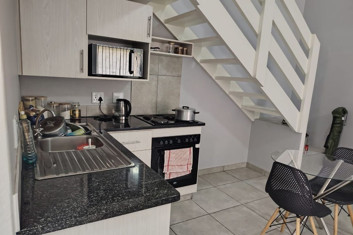 Compact kitchen featuring granite countertops, built-in cabinetry, integrated oven and hob, and tiled flooring, conveniently located beneath a staircase.